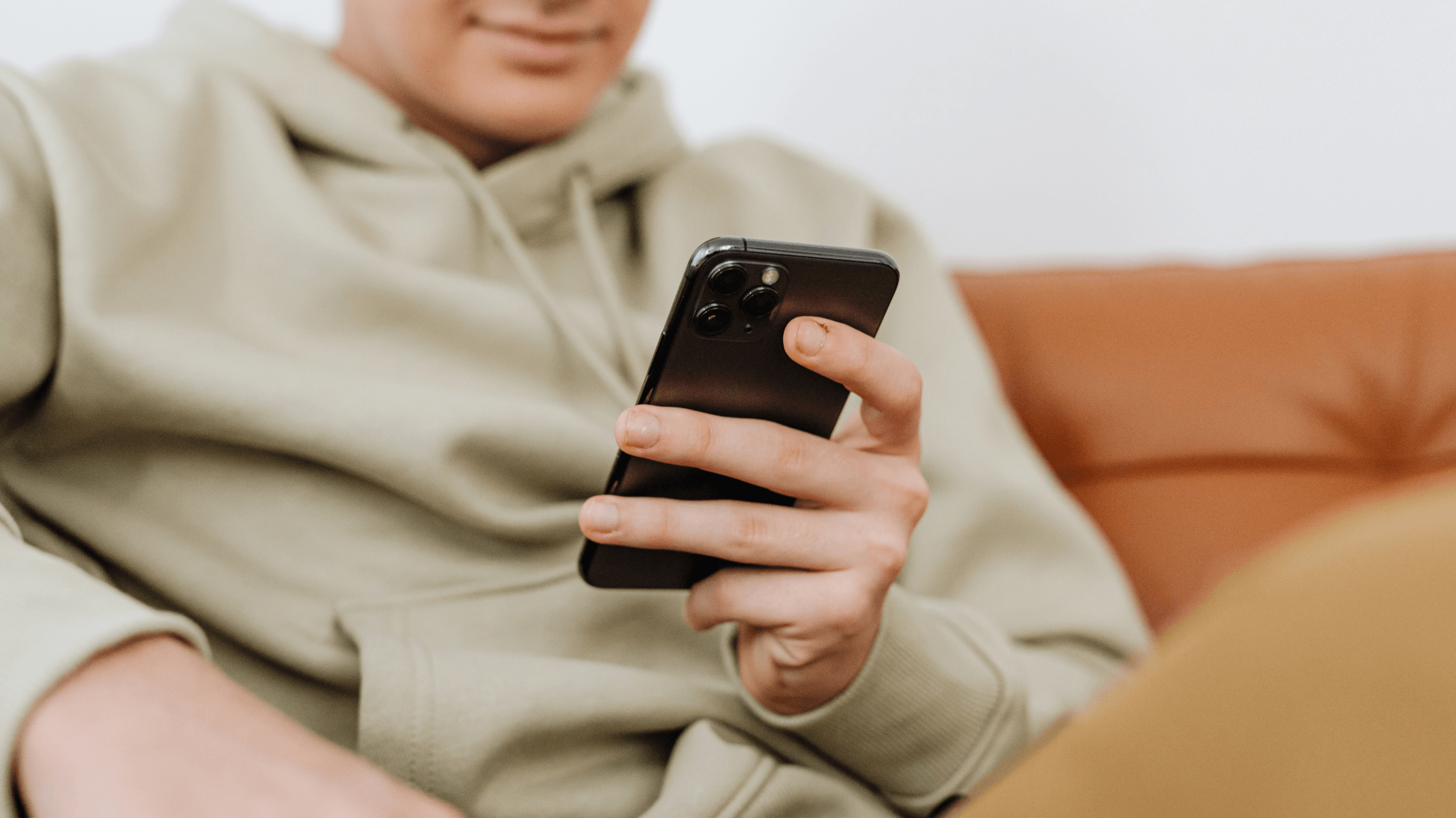 Focused shot of a man of color in a jacket, sitting on a sofa and using a mobile phone, face not visible.