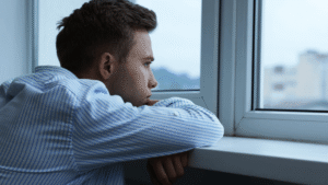 Man looking out window quietly, appearing deep in thought